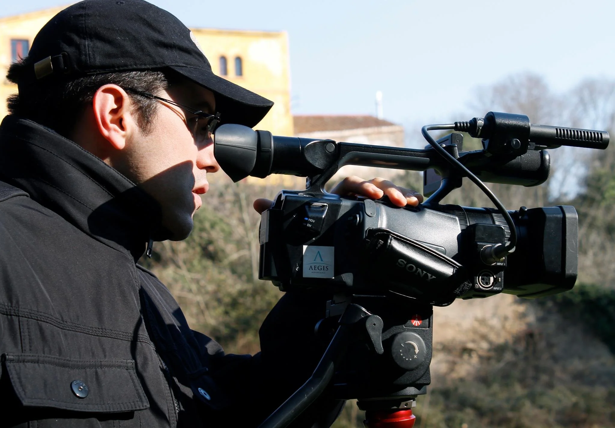 Gerard Pastor wearing a black cap and bundled up, filming in an outdoor setting.